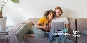 a woman in a yellow shirt sitting next to a man in a white shirt on a couch looking at a laptop together.