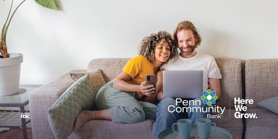 a woman in a yellow shirt sitting next to a man in a white shirt on a couch looking at a laptop together.